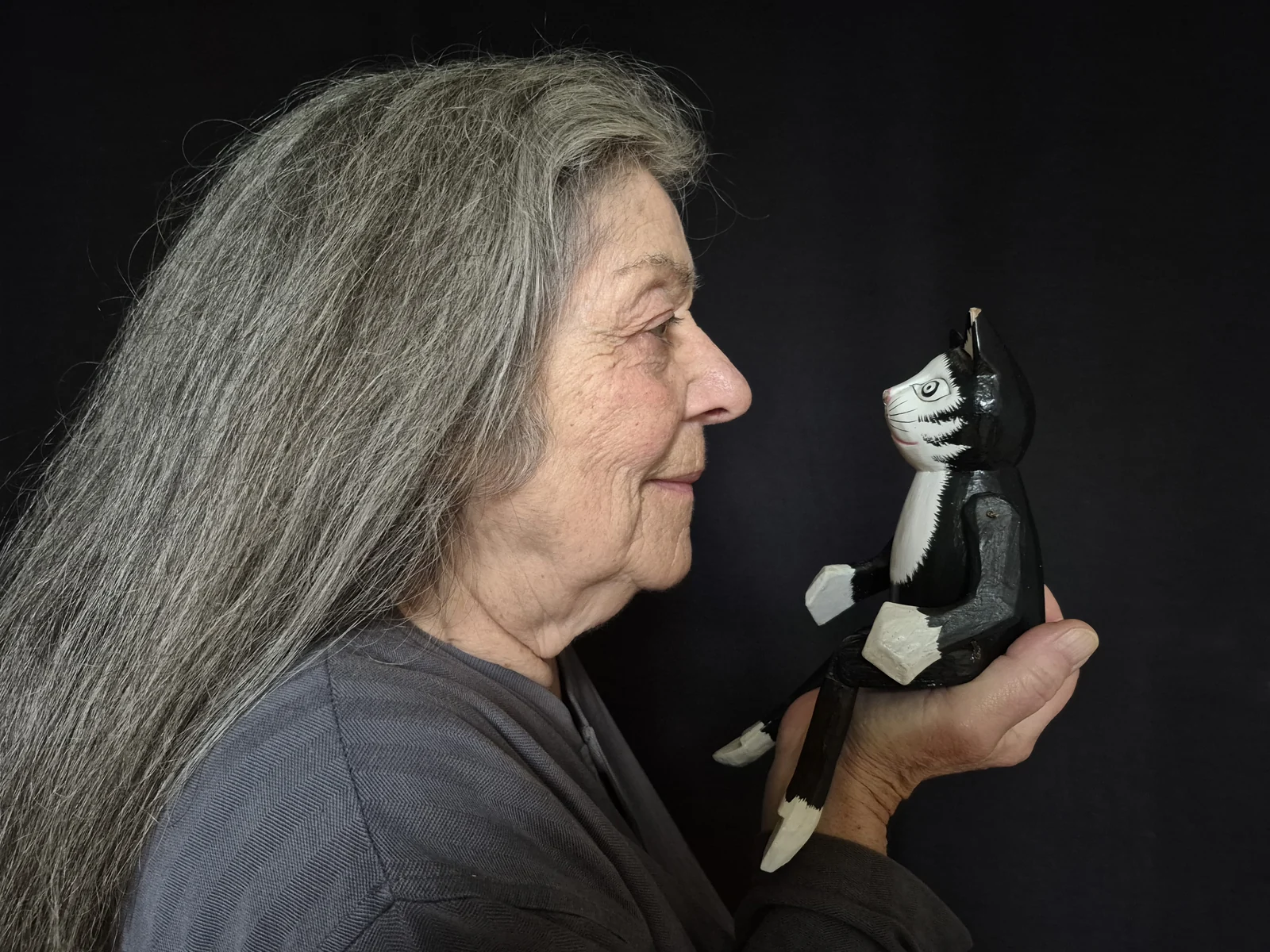 Une femme aux cheveux gris regarde une petite figurine qu’elle tient dans sa main.